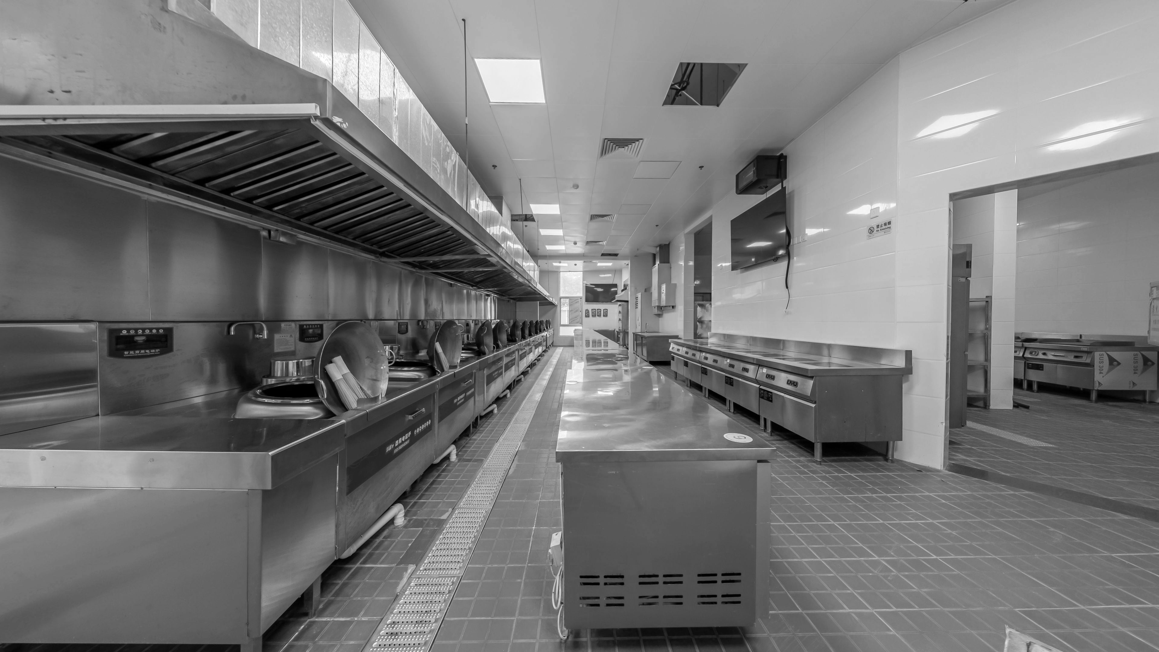 An empty professional kitchen organized around stainless-steel stations and a central work line